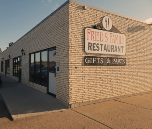 Exterior of Fried's Family Restaurant, featuring a sign for the restaurant and a gifts and pawn shop. Clear blue sky.