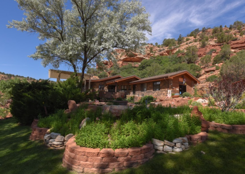 A modern house surrounded by lush greenery and rocky hills under a clear blue sky.