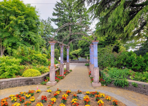 A garden pathway with colorful flowers and an archway framed by lush greenery.