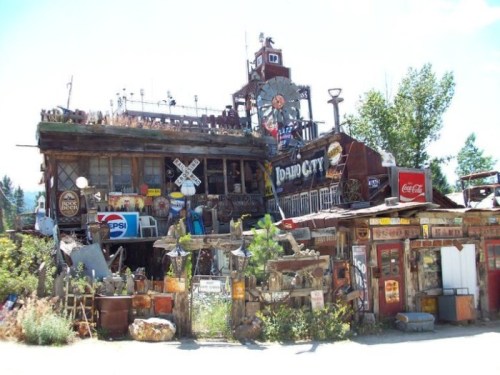 A quirky, eclectic building adorned with signs, antiques, and rustic decor, surrounded by greenery and blue skies.