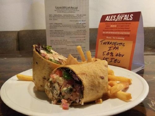A plate with a chicken wrap filled with vegetables, served with fries and a sign for Therapeutic IPA beer.
