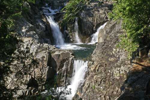 A serene waterfall cascading over rocky cliffs, surrounded by lush green trees and clear water pools.