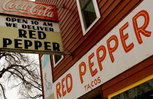 Sign for "Red Pepper Tacos" with delivery info, featuring a Coca-Cola logo and a colorful exterior.