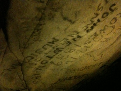 Close-up of a stone surface with various inscriptions and markings, partially illuminated.