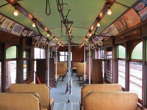 Interior of a vintage train car with wooden benches, overhead lights, and vintage advertisements on the walls.