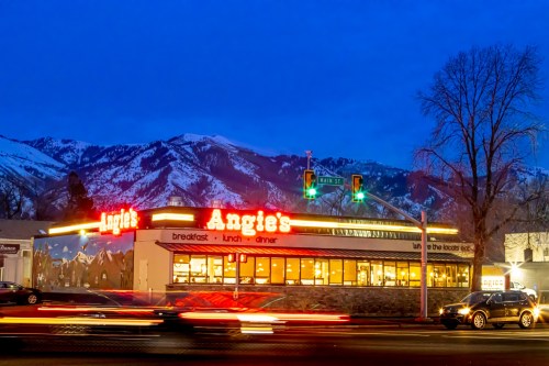 A diner named Angie's illuminated at dusk, with mountains in the background and traffic passing by.