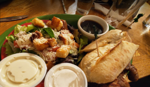 A plate with a sandwich, salad topped with croutons, and two dipping sauces on a wooden table.