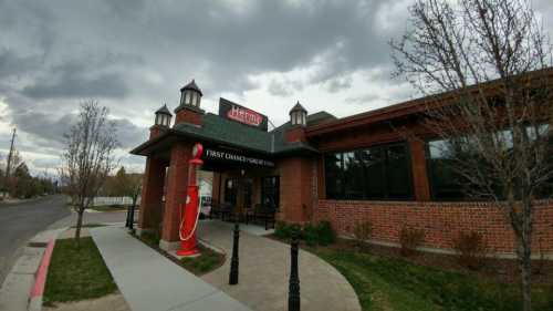 Exterior of a restaurant with a red vintage gas pump, brick facade, and cloudy sky in the background.