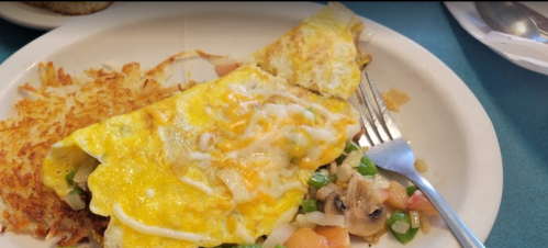 A plate with a cheese omelet, diced vegetables, and hash browns, with a fork resting beside it.