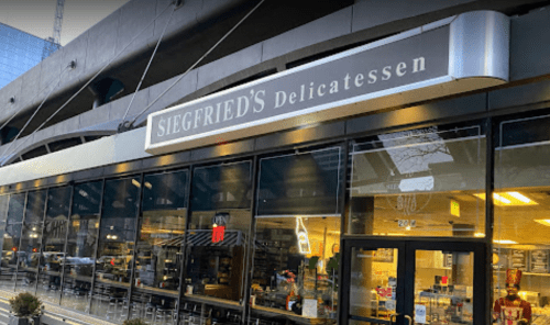 Exterior of Siegfried's Delicatessen, featuring large glass windows and a modern sign, in an urban setting.