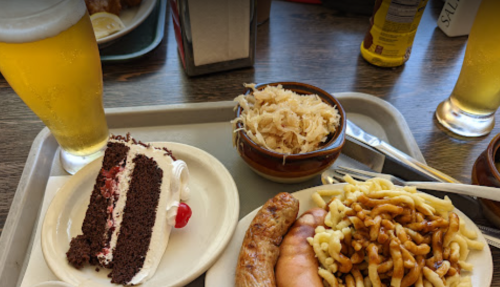 A tray with a slice of chocolate cake, sausage, noodles, sauerkraut, and two glasses of beer.