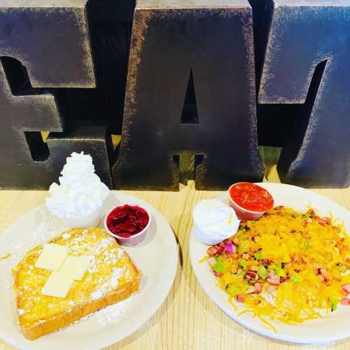 A plate of French toast with butter and syrup, alongside a plate of cheesy nachos with toppings and sauces.