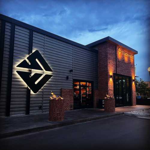 Exterior of a modern building with a lit sign reading "Slackwater" and decorative lighting at dusk.