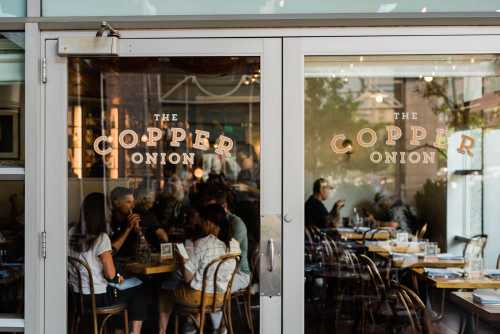 Glass doors of The Copper Onion restaurant, reflecting diners inside and showcasing a warm, inviting atmosphere.