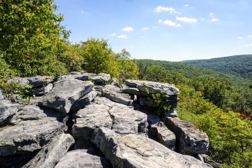 Rocky outcrop overlooking a lush green valley under a clear blue sky with scattered clouds.