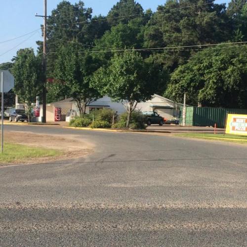 A rural intersection with trees, a few buildings, and a green shipping container in the background.