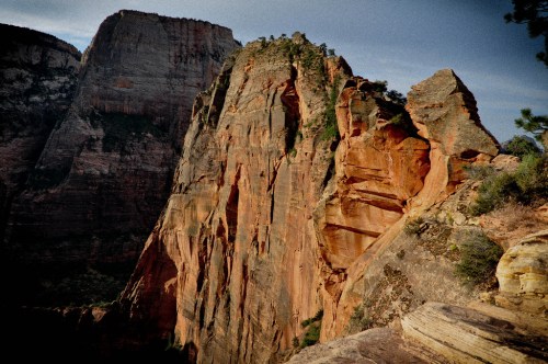 A rugged red rock formation rises sharply against a clear sky, showcasing the natural beauty of a canyon landscape.