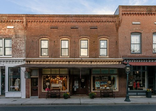 A charming brick storefront with an "ART POINT" sign, featuring large windows and decorative planters outside.