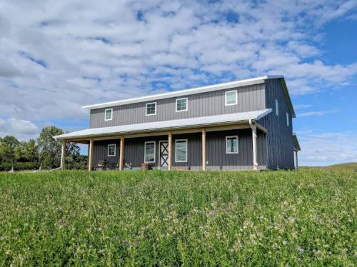 A modern two-story house with a gray exterior, surrounded by green grass and under a partly cloudy sky.
