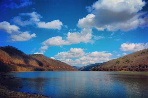 A serene lake surrounded by mountains under a blue sky with fluffy clouds.