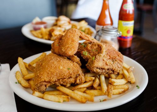A plate of crispy fried chicken served with golden French fries, accompanied by ketchup and hot sauce in the background.