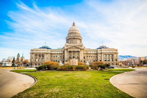 A grand government building with a large dome, surrounded by green grass and blue skies.