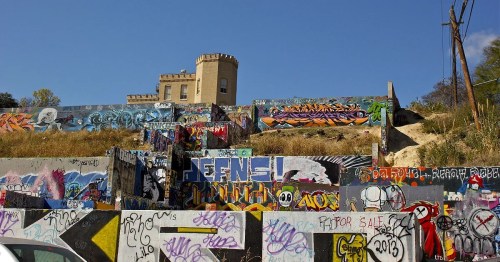 A colorful graffiti-covered wall with a castle-like structure in the background against a clear blue sky.