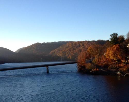 A serene river scene with autumn-colored hills and a bridge crossing over the water under a clear blue sky.