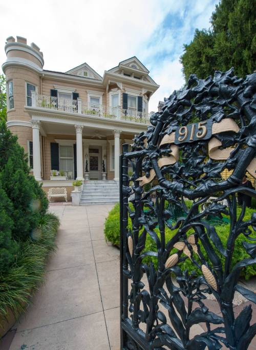 A grand historic mansion with a decorative gate, surrounded by lush greenery and a stone pathway.