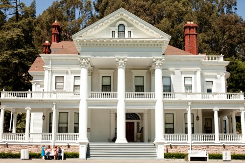 A large, white Victorian-style mansion with columns and a red roof, surrounded by trees.