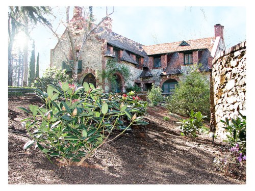 A charming stone and brick house surrounded by lush greenery and colorful flowers in a sunny garden setting.