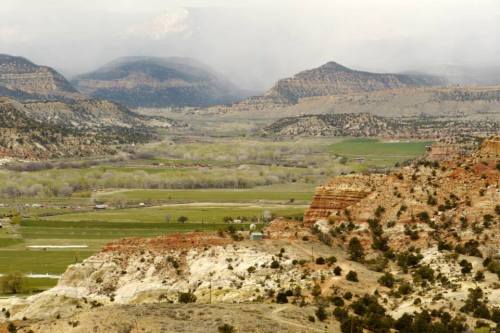 A scenic view of layered mountains and valleys, with green fields and a cloudy sky in the background.
