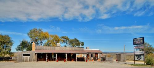 A rustic building with wooden exterior and a sign, set against a clear blue sky and open landscape.