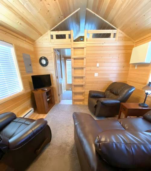 Cozy wooden interior of a small cabin with a TV, two leather chairs, and a lofted sleeping area.