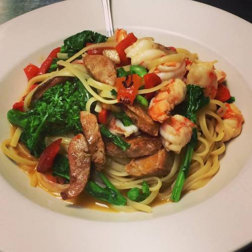 A plate of linguine topped with shrimp, sausage, red peppers, and broccoli in a savory sauce.