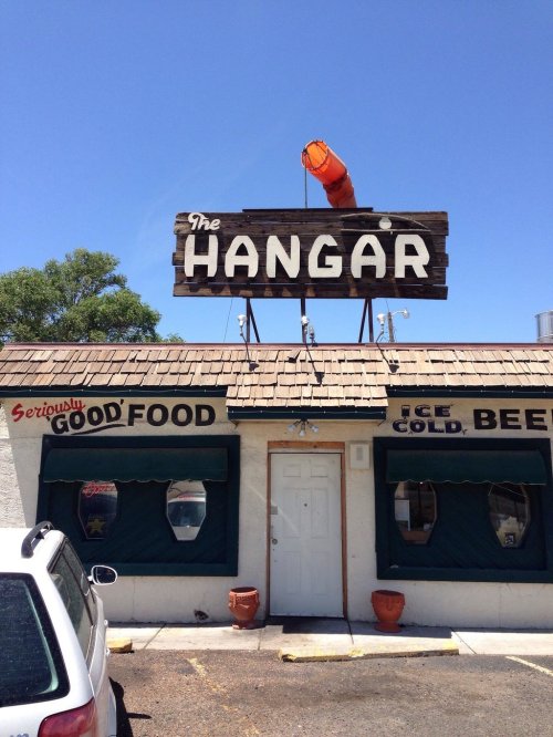 A rustic building with a sign reading "The Hangar," featuring a bright orange object on the roof and a welcoming entrance.