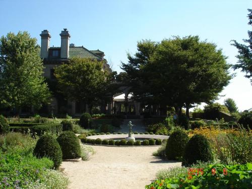 A grand mansion surrounded by lush gardens and neatly trimmed hedges under a clear blue sky.