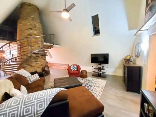 Cozy living room with a stone column, spiral staircase, TV, and comfortable seating. Bright and modern design.