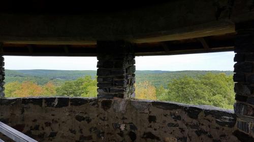 View from a stone lookout tower, showcasing rolling green hills and trees under a clear sky.