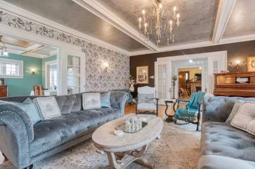 Elegant living room with plush gray sofas, a round coffee table, and decorative wallpaper, featuring a chandelier above.