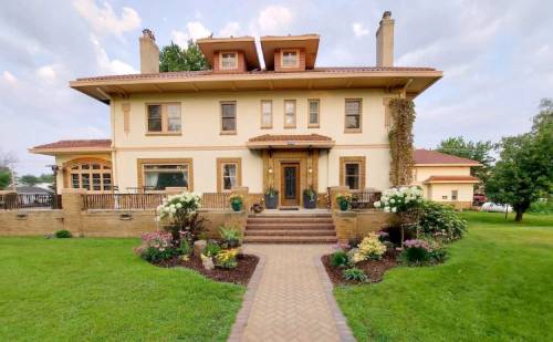 A large, elegant two-story house with a landscaped garden and pathway, featuring a porch and decorative windows.