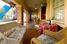 A cozy porch with wicker furniture, a floral tablecloth, and a bottle of wine, surrounded by a welcoming atmosphere.