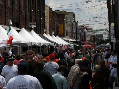 A bustling street festival with crowds, tents, and colorful decorations, showcasing a lively community atmosphere.