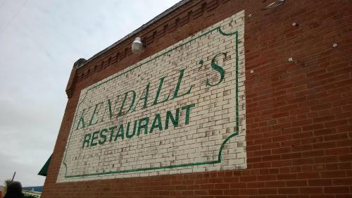 Sign on a brick wall reading "Kendall's Restaurant" in green letters on a white background.