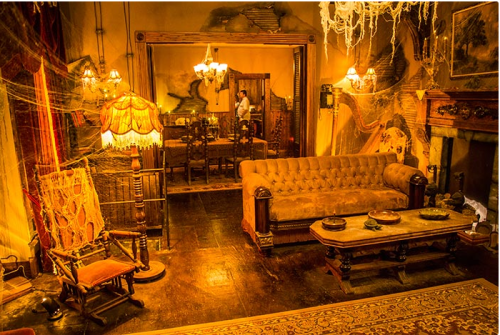 A vintage living room with a brown sofa, wooden furniture, and cobwebs, creating a cozy, eerie atmosphere.