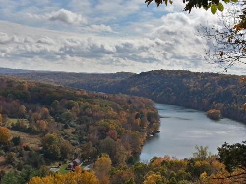 A scenic view of a river winding through colorful autumn foliage and rolling hills under a cloudy sky.