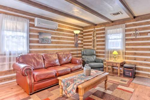 Cozy living room with a leather sofa, armchair, wooden coffee table, and rustic log walls. Warm lighting creates a welcoming atmosphere.