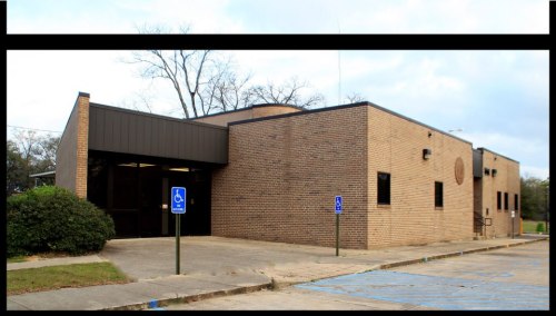 A brick building with a flat roof, featuring a parking lot and accessible parking signs.