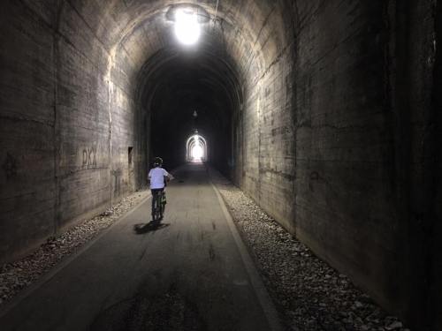 A person on a bicycle rides through a dark tunnel, with light visible at the far end.