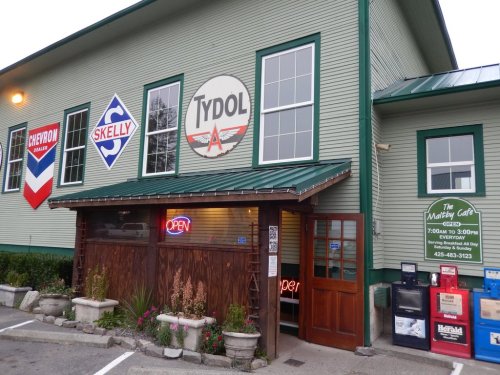 Exterior of a building featuring gas station signs and a café entrance, with an "Open" sign illuminated.